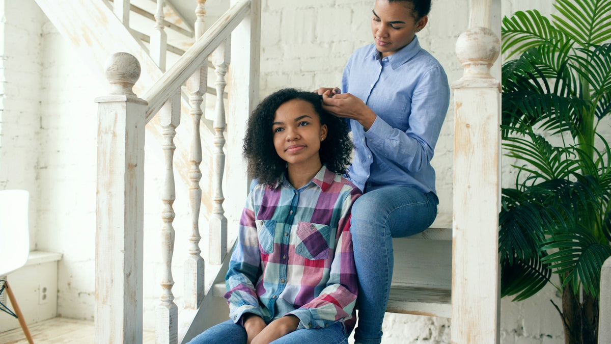 Teen girl sitting on the stairs at home while an older family member braids her hair
