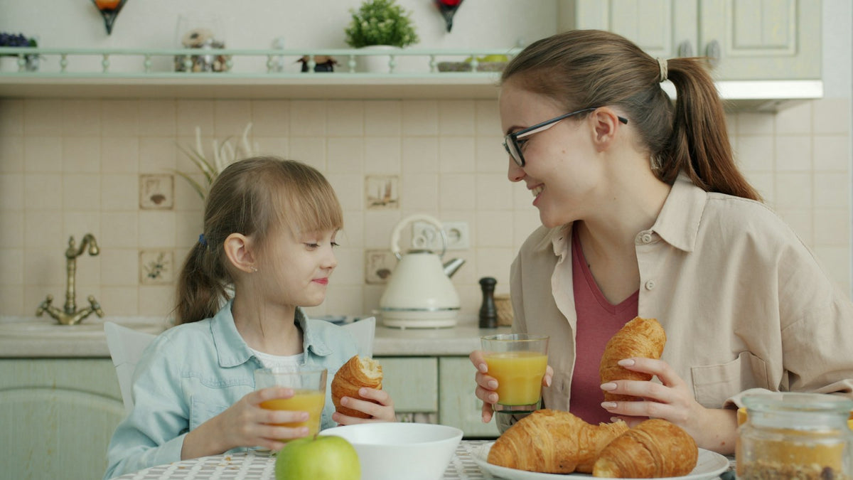 Mother and young daughter eating breakfast together at a bright kitchen table