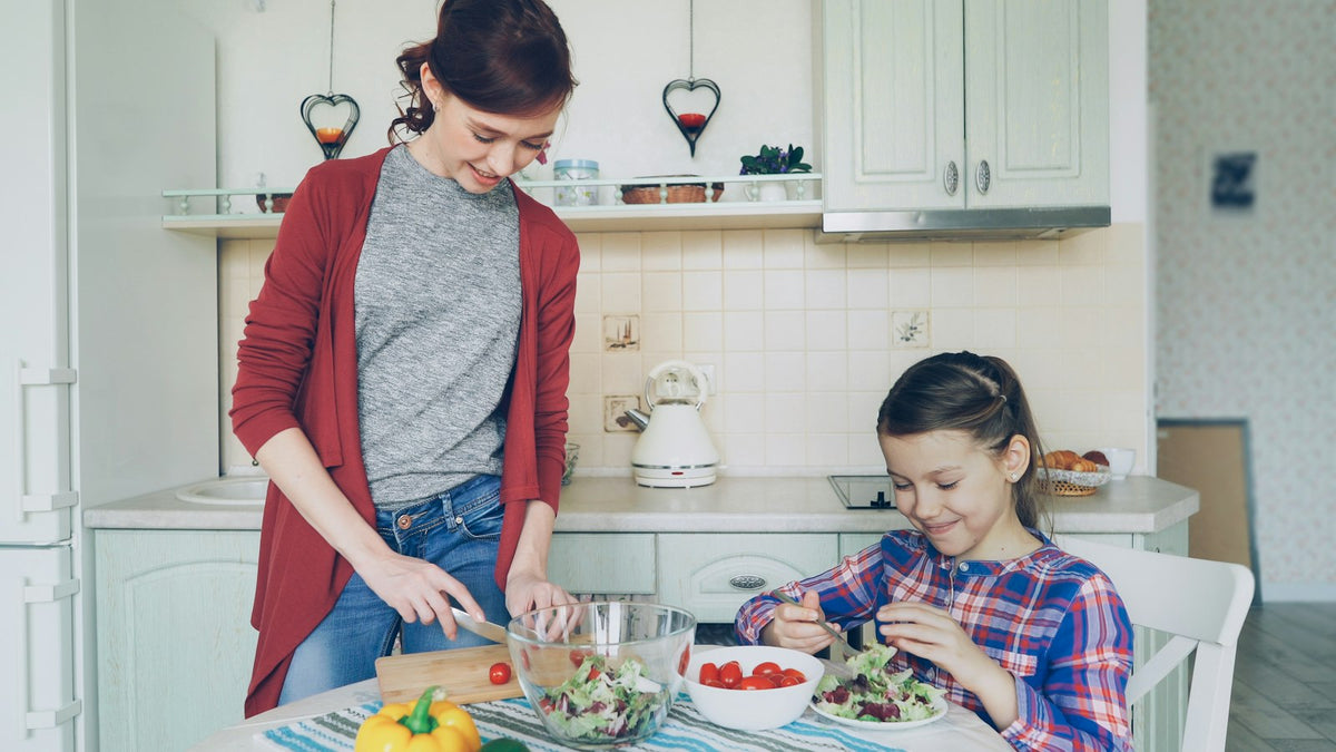 Mother and daughter making a vegetable salad together at the kitchen table