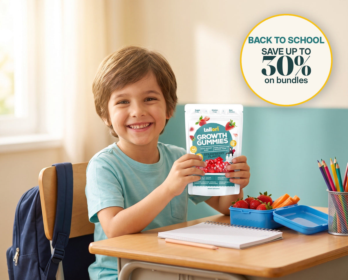 Smiling child at a school desk holding a pouch of Tallori Growth Gummies, with a lunchbox of strawberries and carrots. Back to school: save up to 30% on bundles.